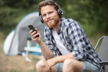 smiling young man tourist using smartphone sitting in tent