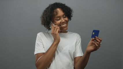 Woman checks creditcard details while holding phone to ear and smiling in studio; confidence empowerment.