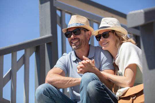 smiling happy couple sitting on stairs at the seaside