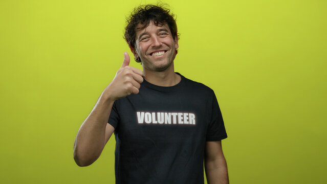 Man smiling confidently with a thumbs-up gesture in front of a yellow background wearing a volunteer t-shirt showcasing positivity and support.