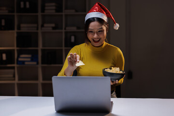 Happy asian woman typing an email on laptop video calling on Christmas at home.enjoy christmas eve weekend xmas celebrate festive seasonal moment.