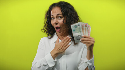 Middle-aged woman holding british pound banknotes against an isolated yellow background, expressing...