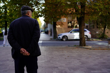 Elderly man stands on sidewalk with hands clasped behind his back in a quiet neighborhood street during the afternoon