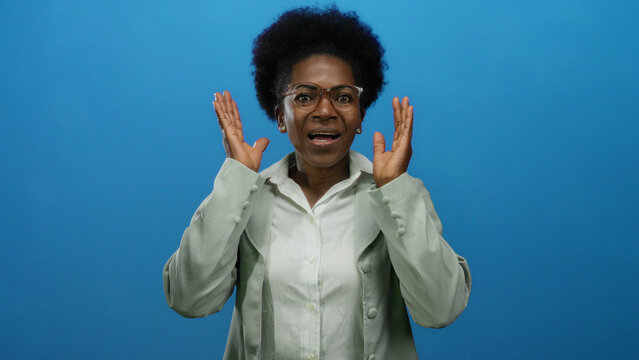 Woman in glasses shows surprise over isolated blue background, communicating emotion, focus, expression, and diversity through visual language and professional attire.