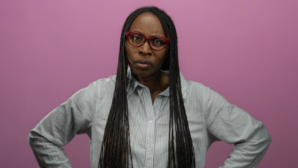 Obraz premium Woman with glasses and braids stands in front of an isolated pink background wall expressing emotion through gesture and gaze