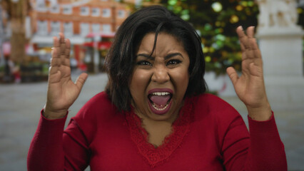 Hispanic woman shouting angrily on a city street, expressing frustration with hands raised, wearing...