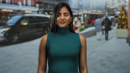 Woman smiling on busy urban street with blurred background, wearing green, showcasing vibrant city life and cultural diversity.