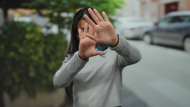 Woman avoiding camera with hands raised expresses discomfort on an urban street.