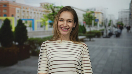 Young caucasian woman with mouth open speaking while wearing a striped top on a paved street; playfulness.