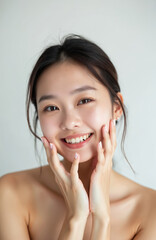 Naklejka premium Young Asian woman touches her soft cheek with a happy smile showcasing clean fresh skin. Her smooth face conveys positive emotion and beauty, isolated on white.