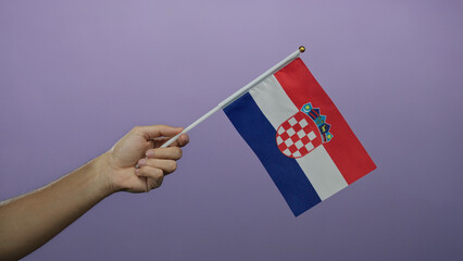 Hand holding croatian flag against purple wall represents national pride and identity, highlighting...