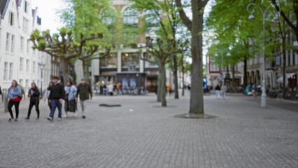 People walking in a blurred european city street with trees, showcasing urban life and outdoor ambience in a bustling town square. © Krakenimages.com