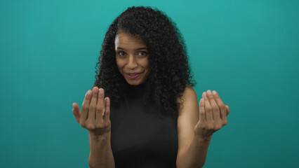 Young hispanic woman with open palms beckons in studio against teal wall with warm smile; friendly...