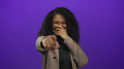 Woman pointing with laughter on a purple background, implying a playful and humorous moment, wearing stylish glasses and a fashionable blazer