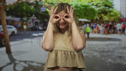 Fototapeta premium Woman makes hand binoculars over eyes wearing beige crop top on busy city street with pedestrians nearby; playful curiosity.