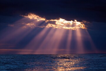 Sunlight pierces dark clouds casting rays over water creating a scene of light and contrast