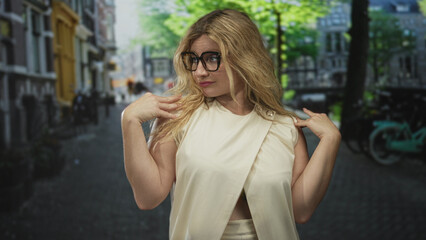 Fototapeta premium Woman with hands on shoulders on a cobblestone street wearing glasses and cream sleeveless top and natural hair; confidence ease.