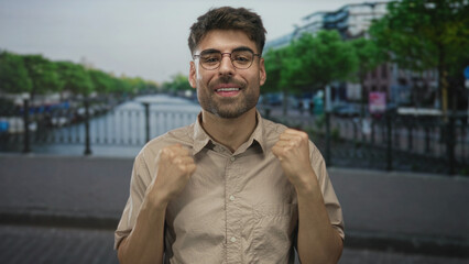 Young hispanic man wearing beige shirt pointing finger to chest on street by canal; pride.