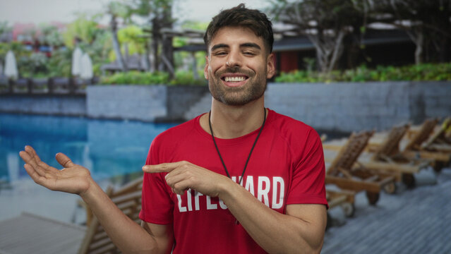 Lifeguard man shows hand ok sign at outdoor resort poolside with whistle around neck; approval confidence.