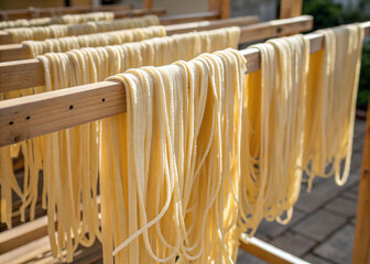 Fresh, golden, homemade Italian pasta, likely fettuccine, air-drying naturally on wooden racks in bright light