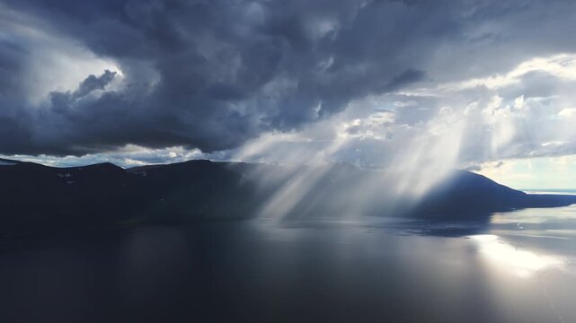 Aerial view of brooding ridges and wide water as sunray pierce the cloud bank. Blue haze drifts across the valley, revealing untouched taiga, long shoreline and a tourism gem in the heart of Siberia