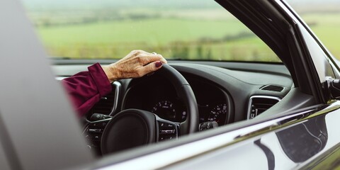 Close-up of a hand on a car steering wheel, with a scenic view outside. The focus is on driving,...