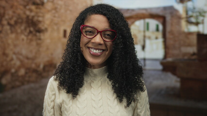 Woman wearing red glasses and cream sweater smiling with visible face in historic street; joyful...