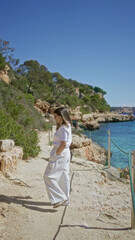 Woman exploring cala llombars beach in mallorca, spain with clear mediterranean waters and rocky cliffs under a sunny sky, creating a picturesque and serene summer scene.