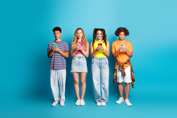 Fototapeta premium fun and friendly teens on a bright blue backdrop absorbed in their phones creating a playful modern youth moment