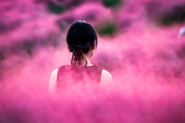 Dreamy moment in pink muhly grass field, woman with black ribbon in soft afternoon light