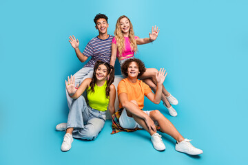 Five friends pose together in bright outfits against a blue background waving hello for a vibrant youth friendship stock photo