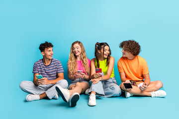 Obraz premium Funny teen friends hangout on a bright blue set chatting and smiling while phones glow with colorful screens in a sunny casual vibe