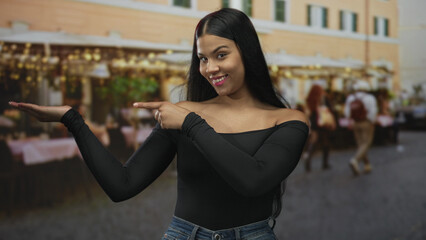 Woman in black top and blue jeans points finger to palm on street outside restaurant terrace; self...
