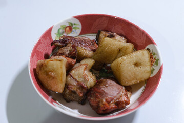 A bowl of traditionally smoked pork, featuring tender chunks of meat with golden, crispy fat layers. The rich brown color shows its slow smoking process, giving it a savory aroma and rustic flavor. 