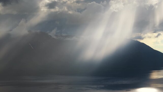 Wide lake mirror catches a narrow sunbeam under towering cumulonimbus above Putorana. Rolling shadow moves along the forest edge, adding grandeur, solitude and a travel mood to the northern scene