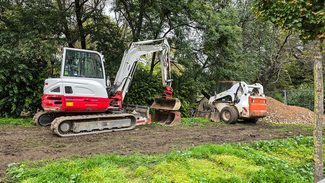 An excavator and a mini loader at a construction site against a background of green trees