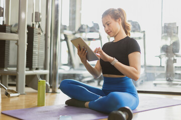 sport healthy asian women sitting in gym fitness using tablet, learning online sports training