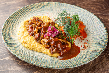 Gourmet dish with creamy polenta, mushroom stew, shredded meat, roasted vegetables, and fresh herbs on ceramic plate. Rustic presentation, ideal for food photography.