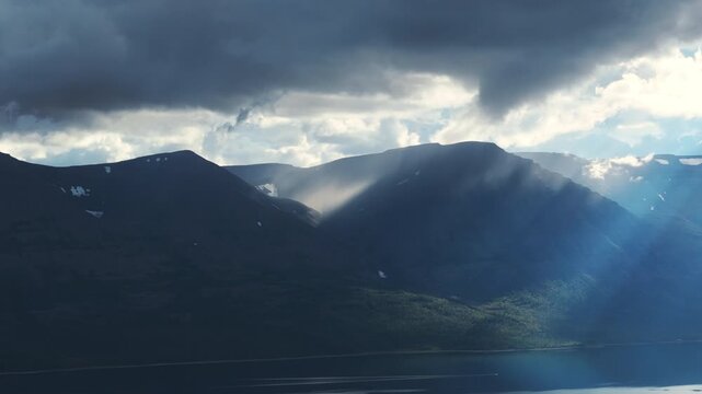 Moody storm cloud breaks above Lake Lama as sunbeam sweeps dark Putorana slopes. Soft haze and shadow create cinematic depth over the taiga shoreline, promising adventure and pristine wilderness