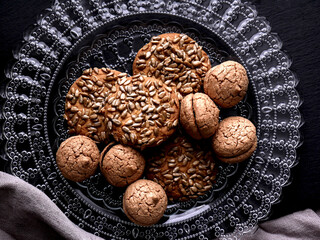 A collection of cookies on a decorative glass plate. The cookies vary in shape and texture, with some appearing to be topped with seeds.