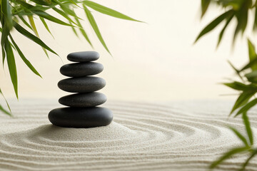 Obraz premium Stacked black stones balanced on sand, surrounded by bamboo leaves in a serene setting