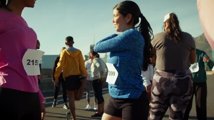 A group of people, wearing race bibs, stretch and warm up before an outdoor running event. They prepare their bodies for physical activity, showcasing dedication and fitness readiness.