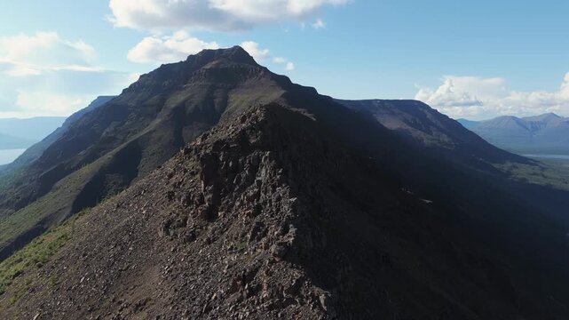 Aerial view follows a rugged ridge toward a pyramid peak above Lake Lama in the Putorana Plateau. Stark relief, volcanic rock and moody light suggest endurance, challenge and authentic wilderness trav