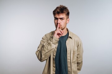 portrait of young man with a thoughtful look, holding his finger to his lips, suggesting the idea of secrecy on white background