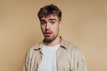 Obraz premium portrait of young man shows a surprised expression, embodying shock and curiosity on beige background