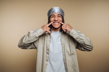 portrait of young man wearing braces, displaying a playful expression while highlighting his bright smile on beige background