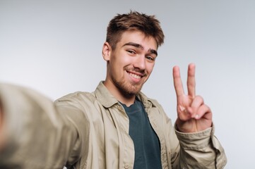 portrait of young man taking a cheerful selfie with a peace sign, radiating joy and playful energy on white background