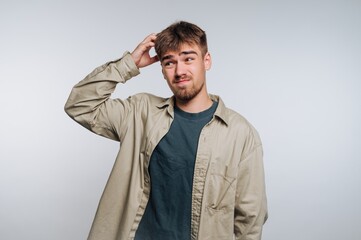 Fototapeta premium portrait of young man scratches his head, showing a confused expression, symbolizing uncertainty and contemplation on white background