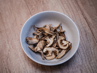 Dried mushrooms in a brown bowl on a wooden table. Natural dehydrated porcini slices prepared for cooking and seasoning.