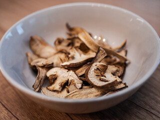 Dried porcini mushrooms in a light brown bowl on a wooden table. Natural dehydrated slices ready for cooking or seasoning.